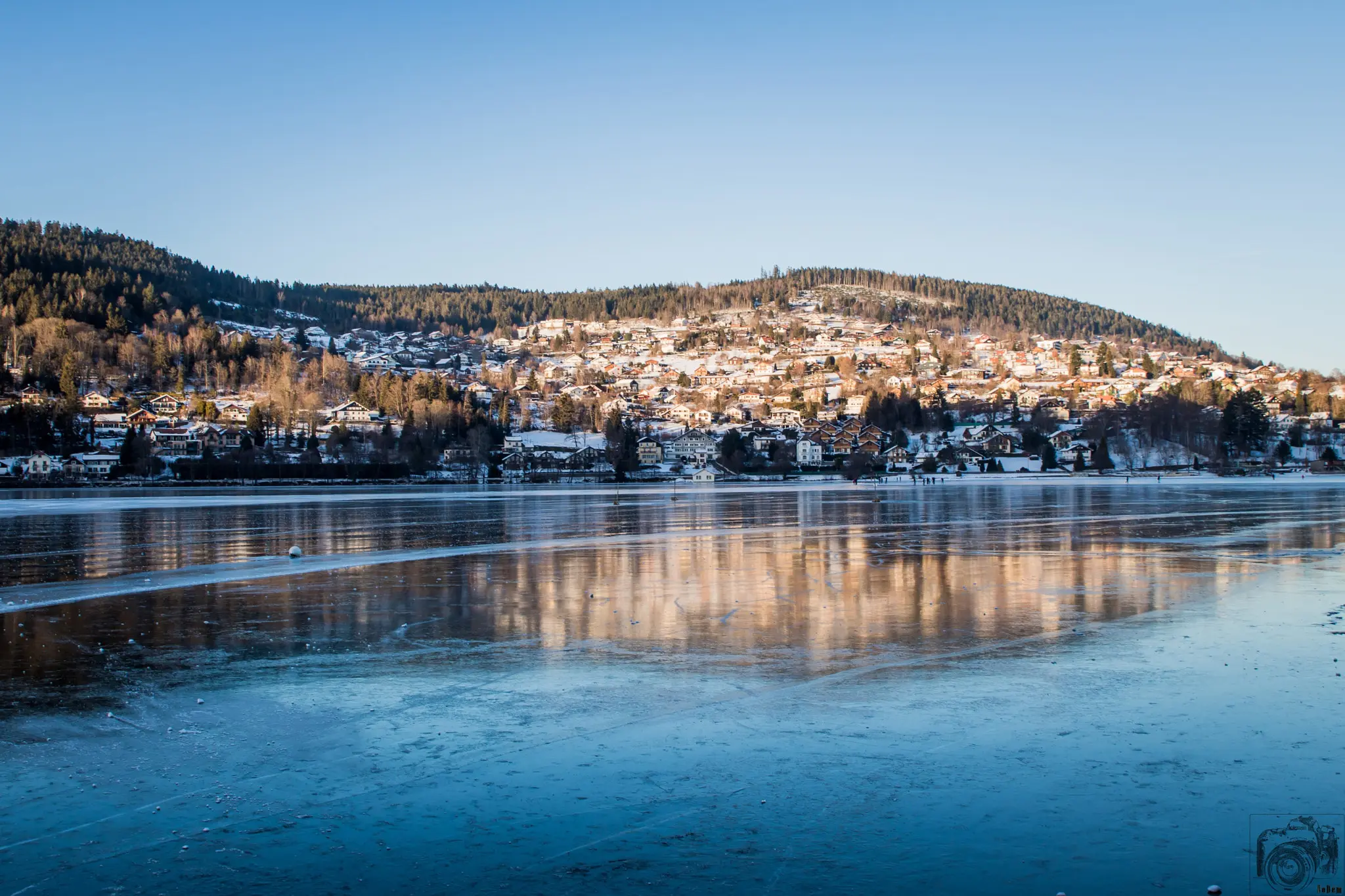 Lac de Gérardmer partiellement gelé devant la ville et les collines enneigées